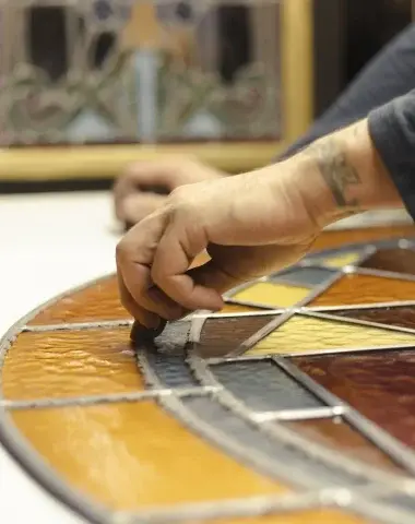 Close-up of an artisan’s hand assembling colorful stained glass pieces in a decorative pattern – traditional craftsmanship in France