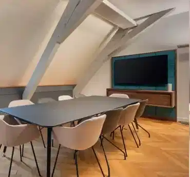 Modern meeting room in Paris with a large table, chairs and TV screen under attic beams