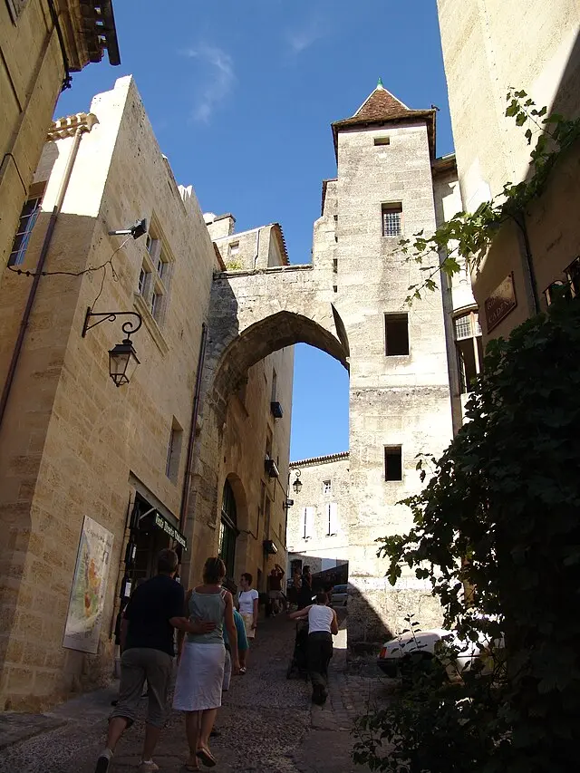 People walking up a medieval street under a stone arch in Saint-Émilion, France