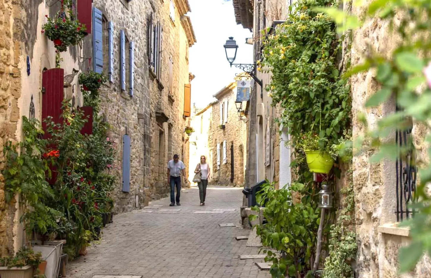 Stone alley with flower pots and shuttered windows in a quiet Provençal village, with two people walking