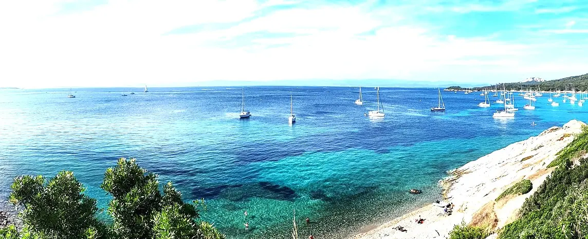 Turquoise Mediterranean waters with sailboats anchored near a rocky beach in southern France