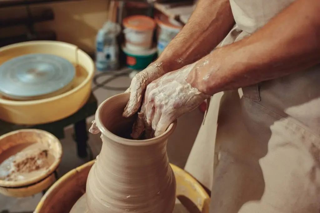 Close-up of a potter shaping clay on a traditional wheel – hands covered in wet clay during ceramic making process