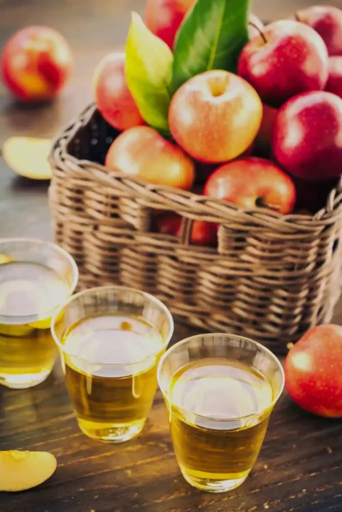 Three glasses of cider in front of a basket full of red and yellow apples – traditional Normandy produce